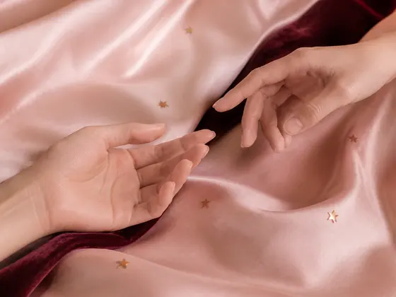 淡いピンクの布の上で、ふたつの手がそっと近づく様子